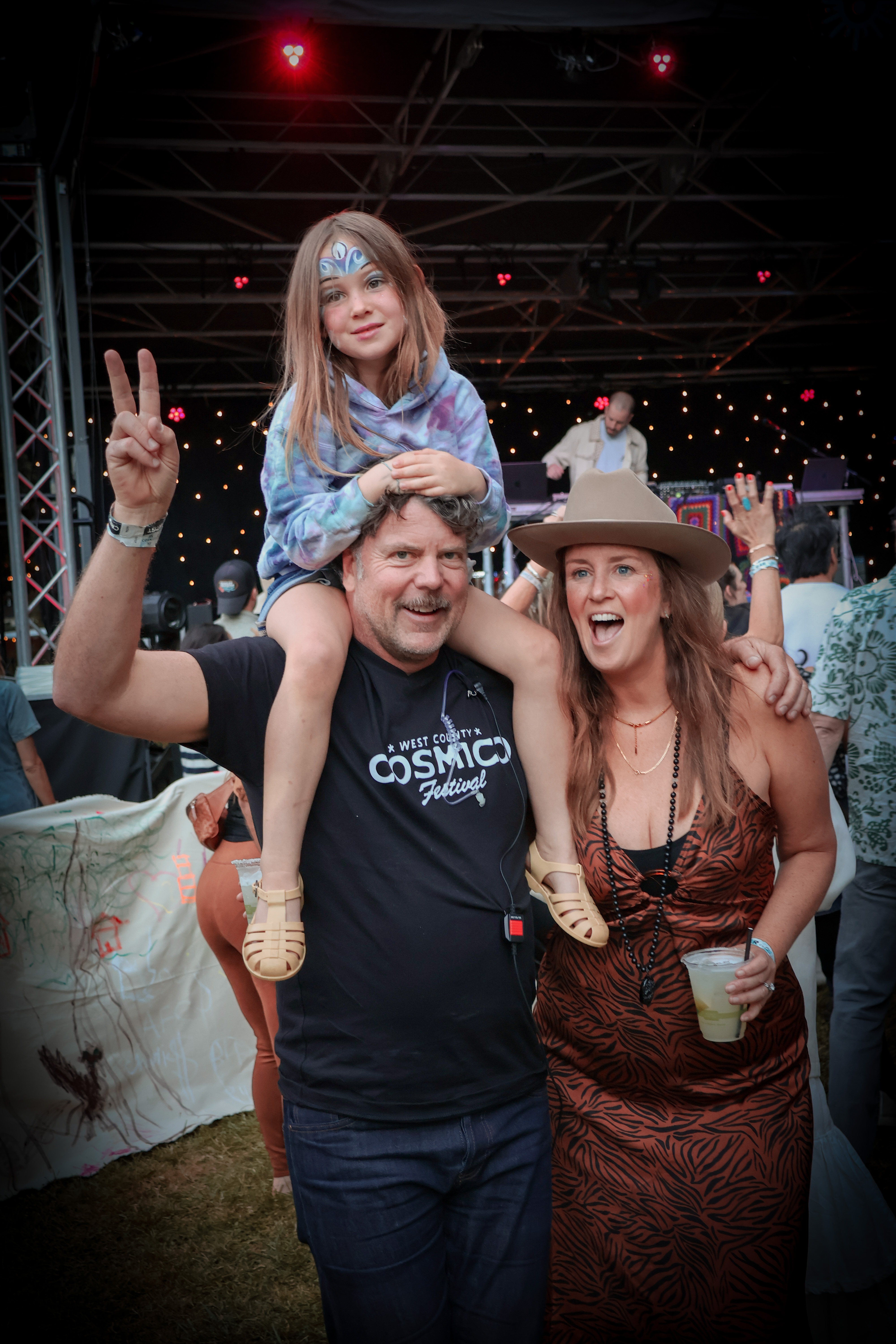 Chris Schultz and Anne Driscoll celebrating at Cosmico with their child on Chris’s shoulders and a raised peace-sign gesture